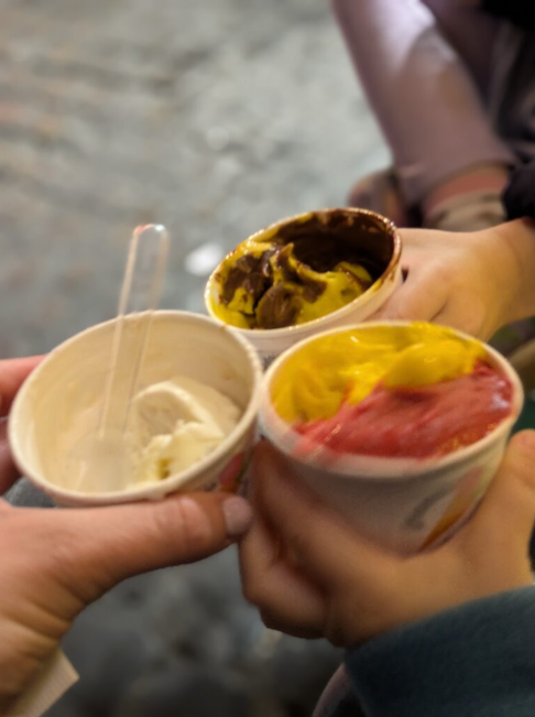 Three hands holding three cups of gelatos in Rome at night.