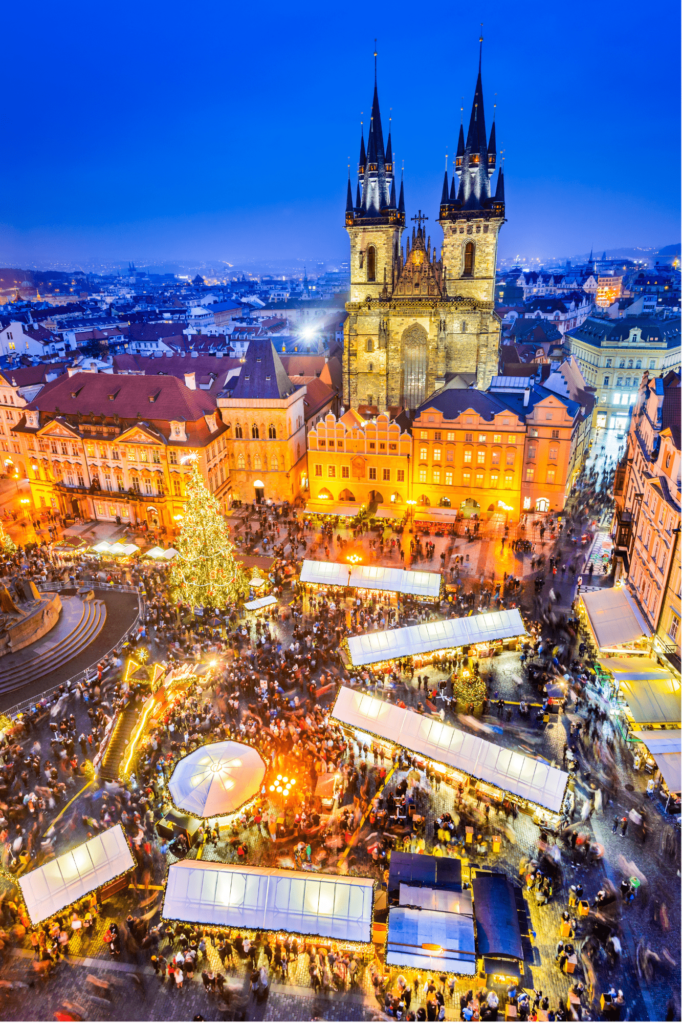 Prague's Christmas market seen from above with the massive lit up Christmas tree and the gothic towers right beside. 