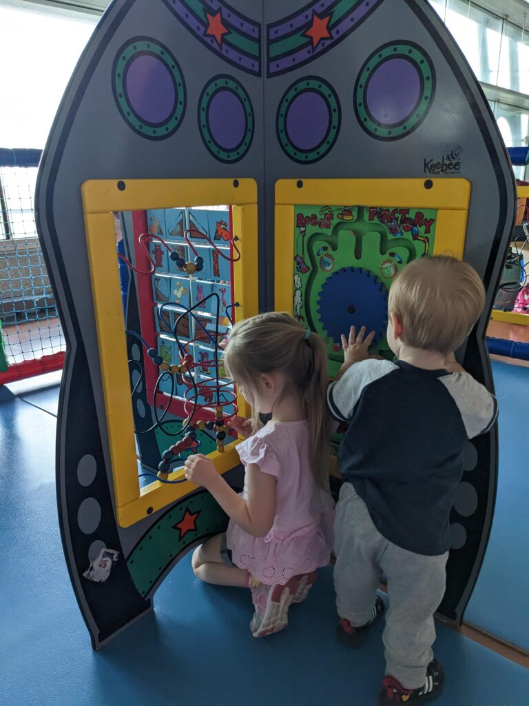 Un tout-petit garçon et une jeune fille s'amusent dans une aire de jeux à l'aéroport avant l'embarquement.