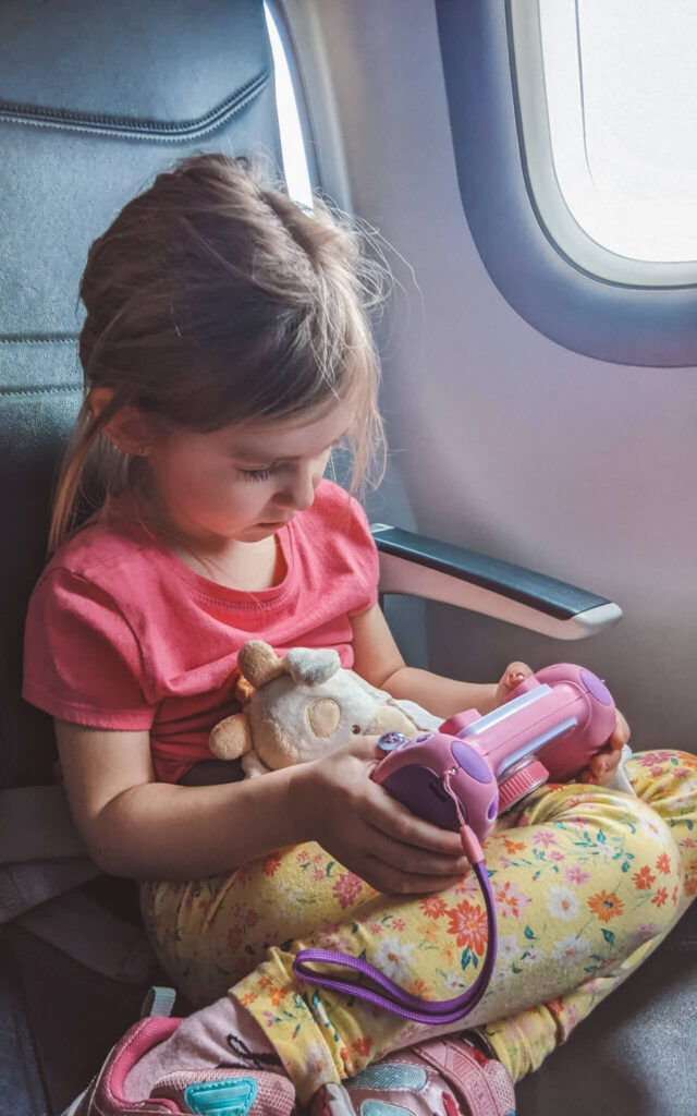 Une petite fille qui joue avec un appareil photo pour enfant Vtech Kidizoom dans l'avion. C'est un jouet simple et amusant à ajotuer au bagage de cabine des tout-petits. 