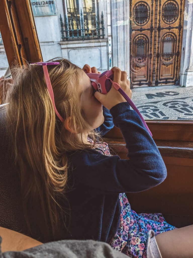 Little girl on a tramway in Lisbon, taking a picture with a pink VTech kid camera.