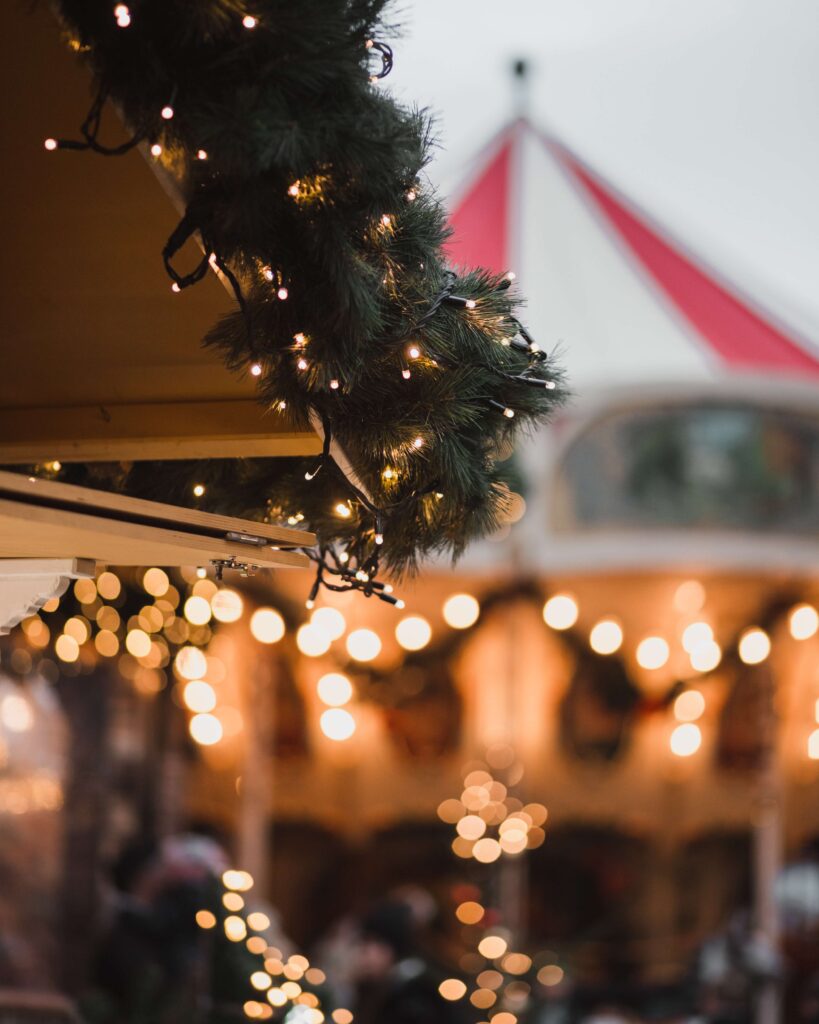 A stand with Christmas lights on a garland in front of a blurred carousel at one of the famous Christmas markets in Europe. 