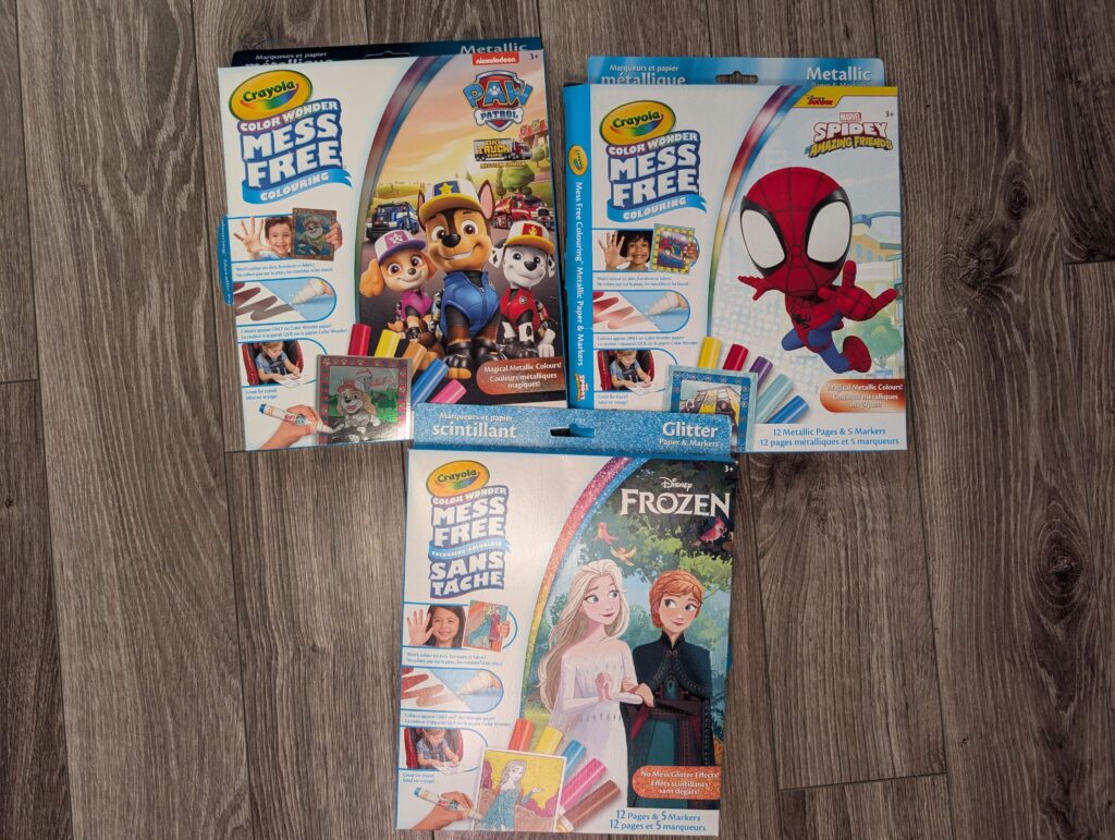 Three boxes of Crayola mess free kits on a hardwood floor. ON the left is a box of Paw Patrol, on the right a box of Spiderman, and under them a box of Frozen.
