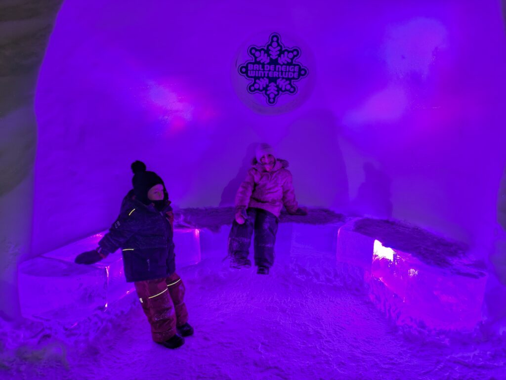 Two kids sitting on ice benches at night with purple lights at Winterlude, Ottawa's winter festival.