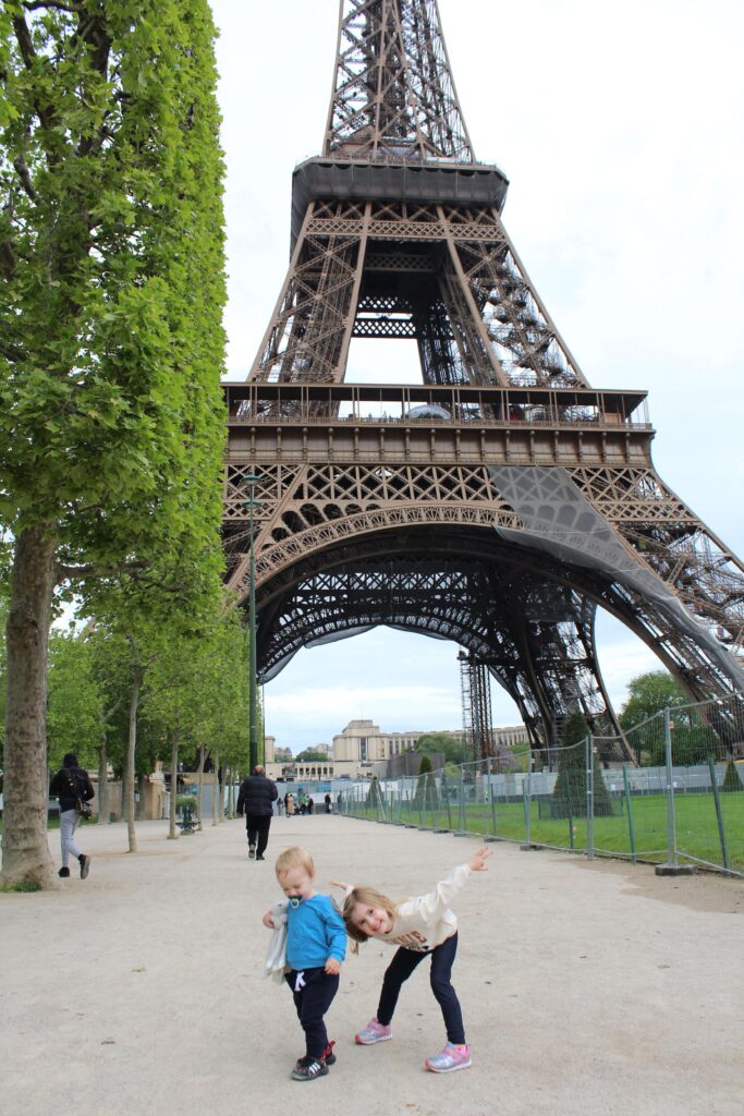 Two kids standing at the base of the Eiffel Tower at Champ-de-Mars in Paris