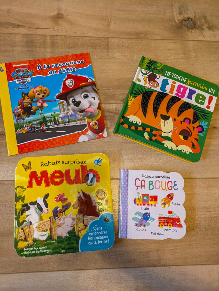 4 colorful books for toddlers on a hardwood floor. Books are underrated airplane toys for toddlers. You should definitely pack a few in your carry-on!