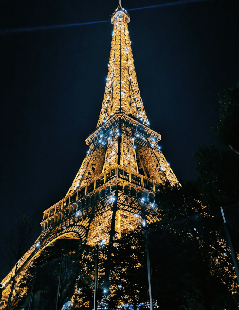 The Eiffel Tower sparkling at night, seen from the ground. It's a must for both kids and parents in Paris
