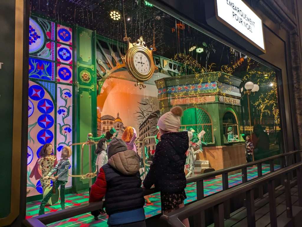 Two kids looking at Christmas decorations in big stores displays in Paris in November.