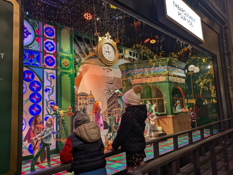 Two small kids in winter clothes looking at the Christmas display at Galeries Lafayette at night in Paris, France.