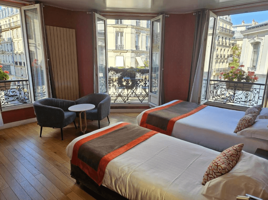 Two twin beds facing opened glass doors in the spacious family room at the Latin Home Hotel in Paris.