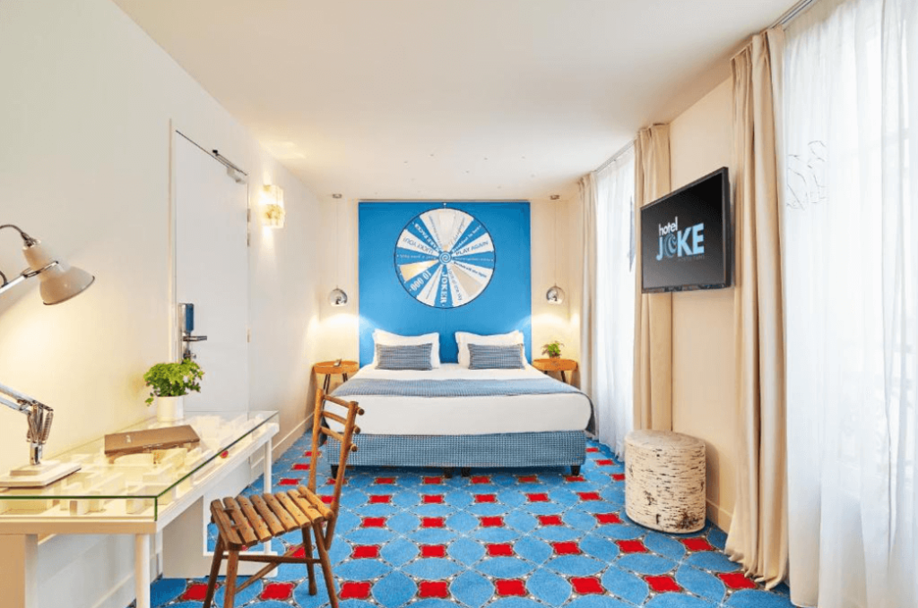 A bright double bedroom at the Hotel Joke from Astotel in Paris. With bright blue walls and carpet, the room has a fun family-friendly atmosphere.