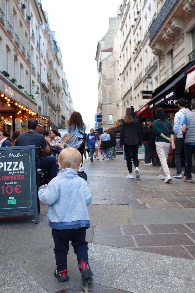 A toddler walking on Montogrgueil Street with the Italian restaurant La Perla's terrace in the background. This is one of the best areas where to stay with kids in Paris since it's a safe neighborhood filled with restaurants and cafes. 