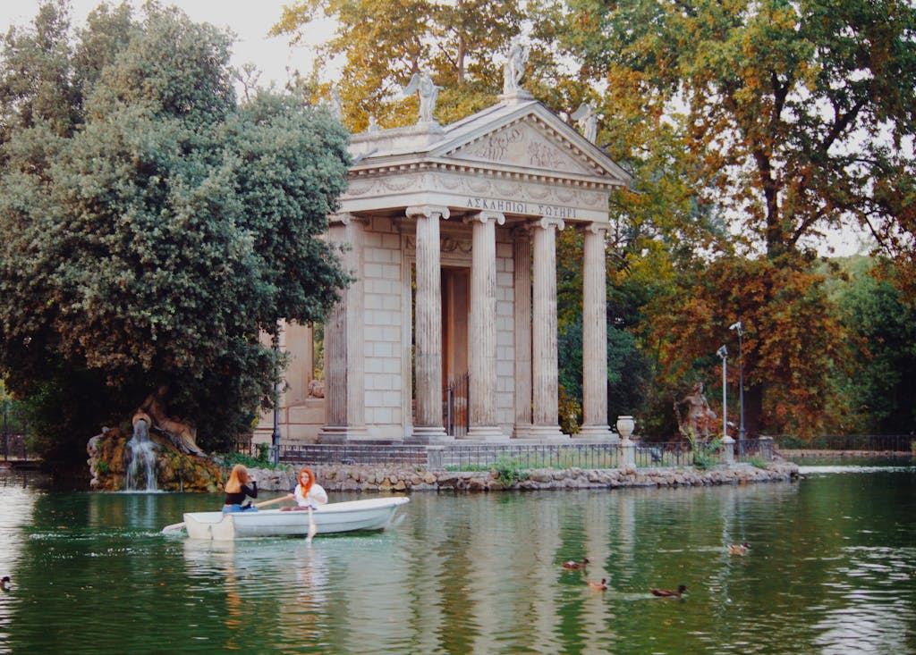 A serene canal scene with a boat navigating by an ancient temple in Rome's Villa Borghese. Villa Borghese in a bit more quiet in the fall.