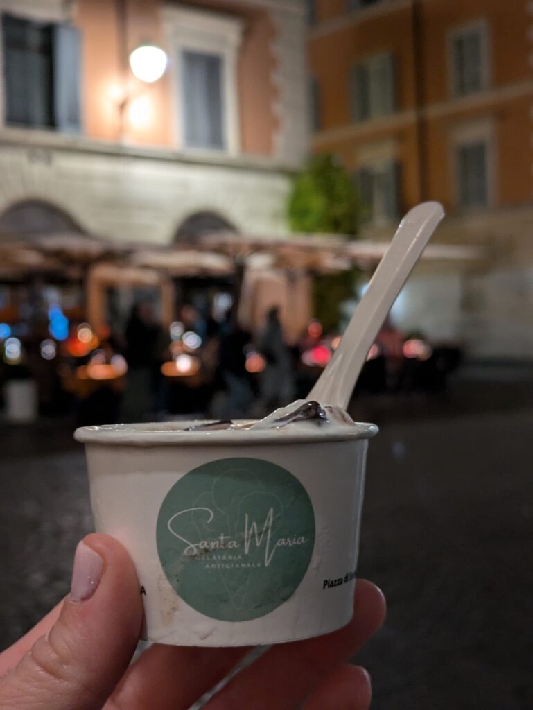 Cup of gelato held in the hand of a woman with light pink nail polish at night in Trastevere, Rome, Italy.
