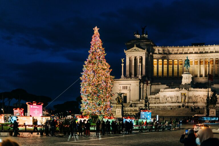 Christmas tree lit up in front of one of Rome's famous landmarks at night.