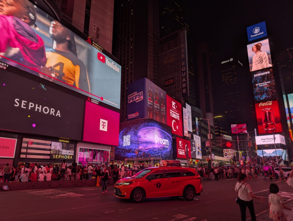 Crowds and yellow taxi on Times Square at night with bright colorful screens. Visiting Times Square at night is one of the top mistakes to avoid in NYC with kids as it's too crowded and loud. 