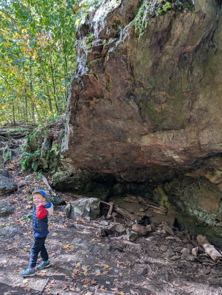 A small kid standing below a big rock on the Sugarbush trail in Gatineau Park