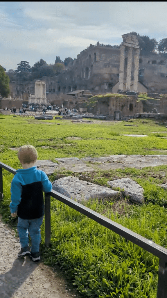 A toddler walking on a stone path with the Roman Forum in the background. Families can opt for a Colosseum tour that also includes access to the Forum.