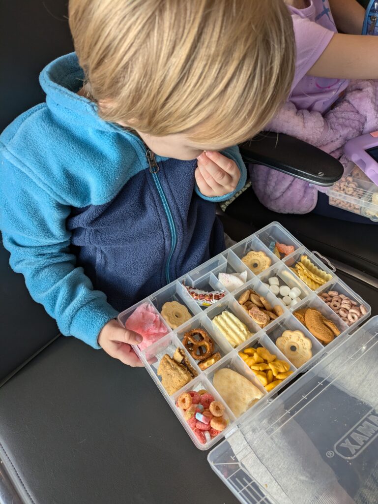 Toddler boy with a blue shirt eating a snack from his surprise snack box at the airport.