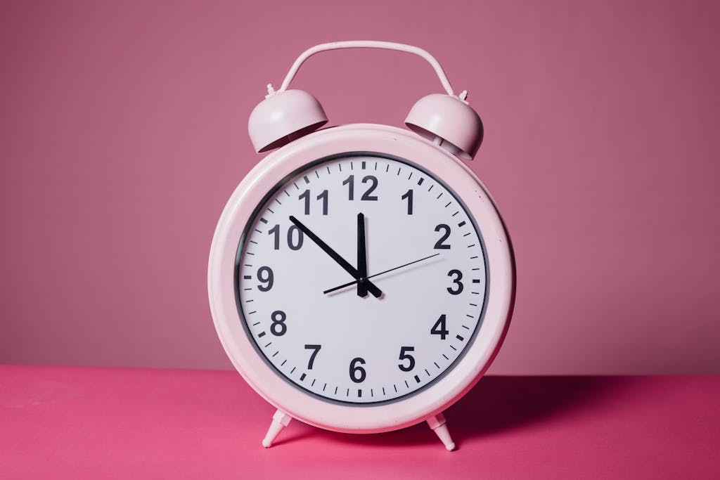 Pink retro alarm clock on a pastel pink background symbolizing time and punctuality. When landing, you'll need to cap the naps to help beat jet lag with kids.