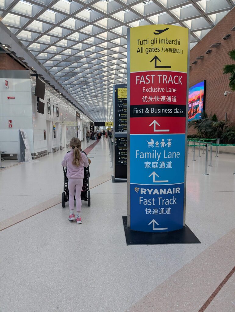 A little girl pushing a stroller towards the family line for airport security in Marco Polo airport in Venice, Italy. You can bring your stroller to the airport security with your kids.