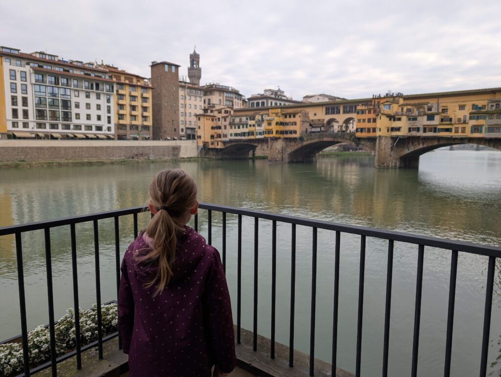 Little girl with a purple jacket standing on a terrace looking at Ponte Vecchio in Florence, Italy. Ponte Vecchio is definitely a must for families in Florence,