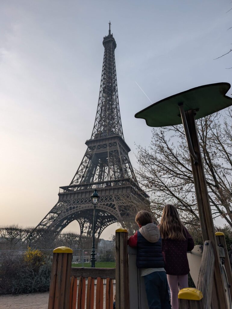 Two kids standing on a playground structure in front of the Eiffel Tower in Paris, France.