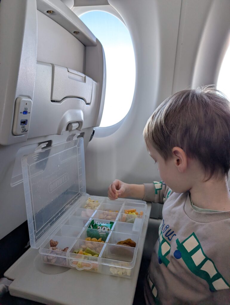 Tout-petit garçon qui sélectionne une collation dans sa boîte à collation dans l'avion. Ces petites boîtes surprises sont parfaites pour organiser les meilleures collations pour l'avion