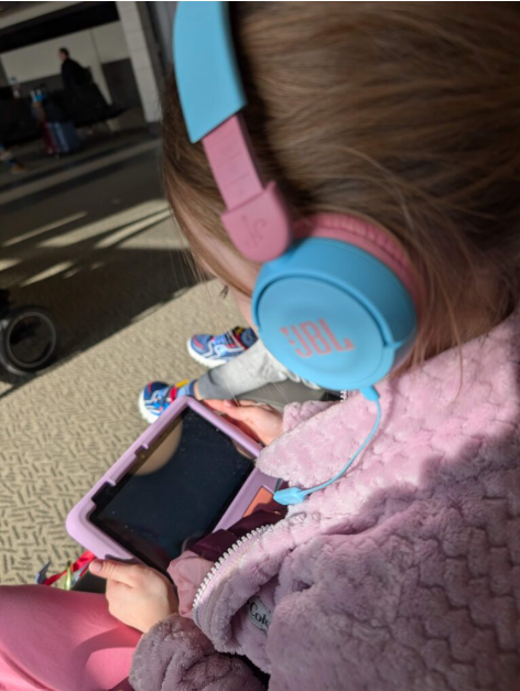 Jeune fille qui regarde sa tablette avec des écouteurs bleu et rose JBL à l'aéroport. 