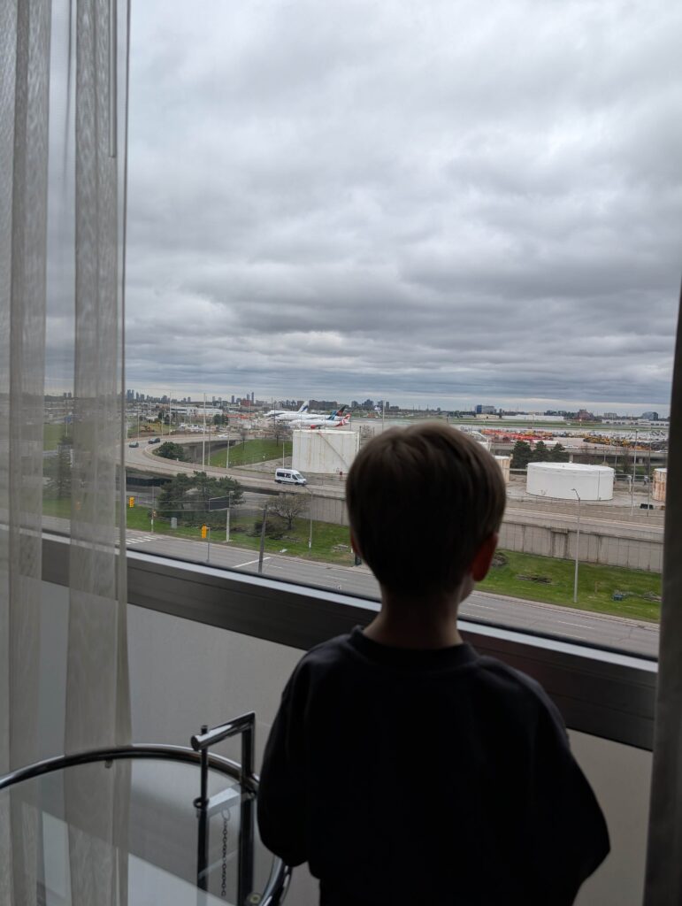 Little boy looking at planes landing and taking off at Toronto Pearson airport through the window of his room at the Hilton Toronto Airport Hotel & Suites.
